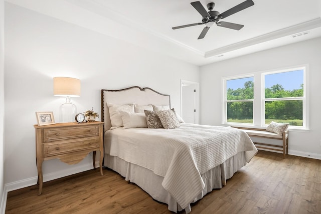 bedroom featuring wood finished floors, a ceiling fan, visible vents, baseboards, and a tray ceiling