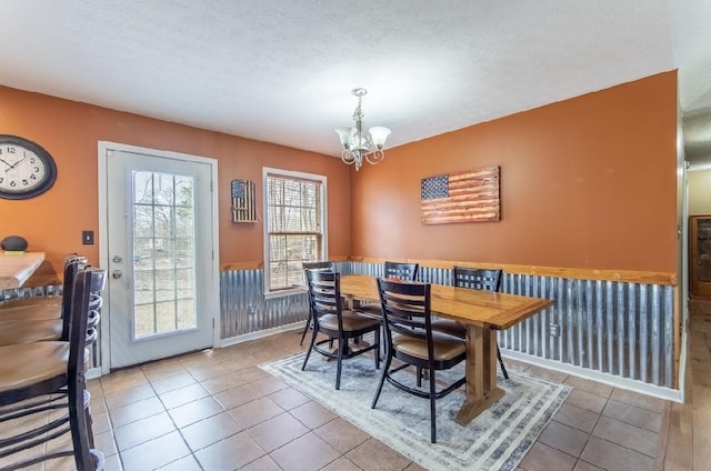 dining space featuring a textured ceiling, a wainscoted wall, tile patterned flooring, and a notable chandelier