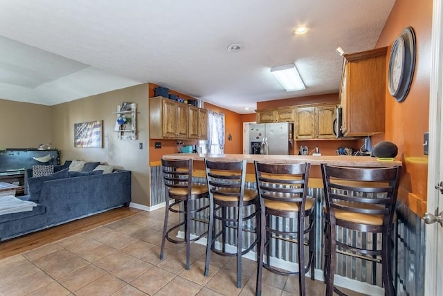 kitchen featuring a peninsula, open floor plan, appliances with stainless steel finishes, brown cabinetry, and a kitchen bar