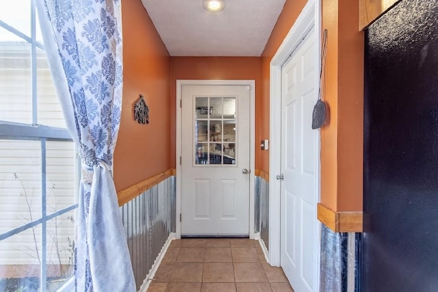 doorway with a wainscoted wall and light tile patterned floors