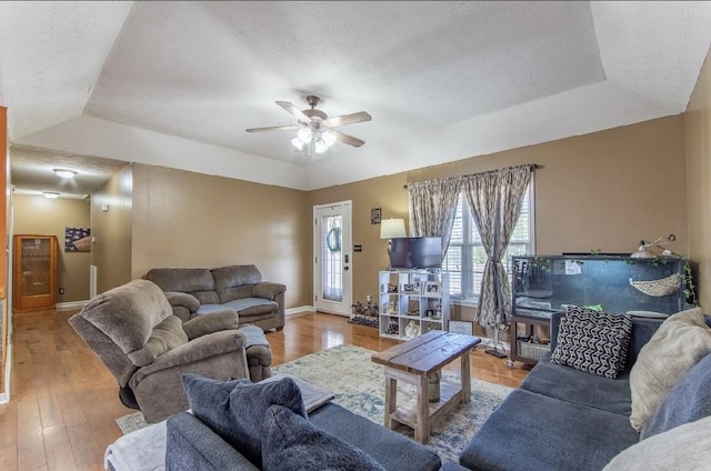 living area with a tray ceiling, ceiling fan, a textured ceiling, wood finished floors, and baseboards