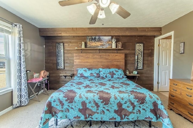 carpeted bedroom featuring wooden walls, an accent wall, a ceiling fan, and multiple windows