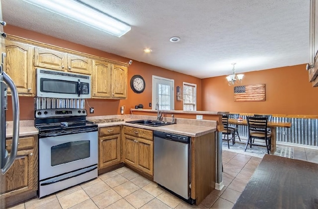 kitchen featuring light tile patterned floors, appliances with stainless steel finishes, a peninsula, light countertops, and a sink