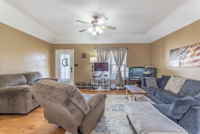 living area featuring light wood-style floors, ceiling fan, and a raised ceiling