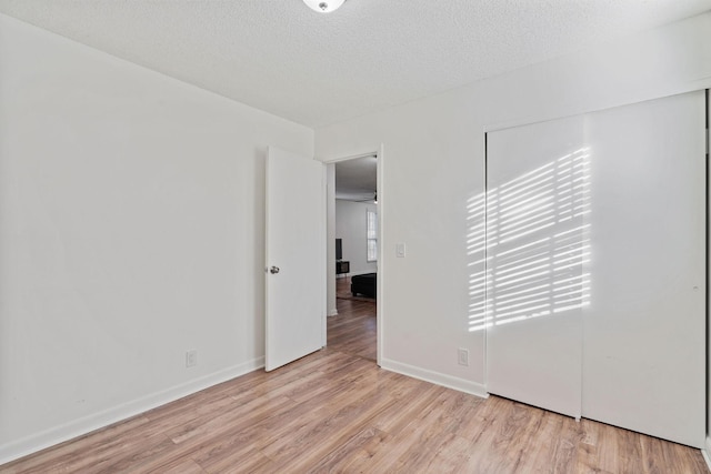 empty room with a textured ceiling, light wood-type flooring, and baseboards