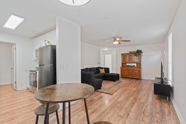 living room featuring a skylight, light wood-style flooring, baseboards, and a textured ceiling