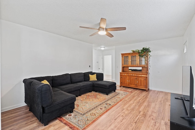 living area with light wood-type flooring, ceiling fan, baseboards, and a textured ceiling