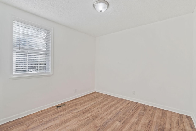 unfurnished room featuring baseboards, light wood-style flooring, visible vents, and a textured ceiling