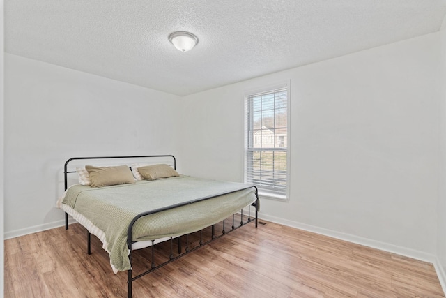 bedroom with a textured ceiling, baseboards, and wood finished floors