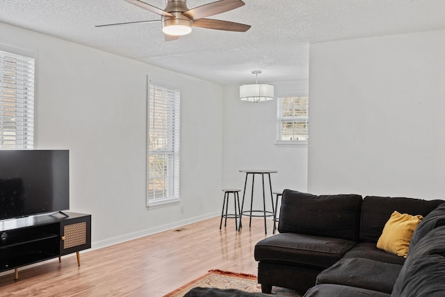 living area with ceiling fan, a textured ceiling, baseboards, and wood finished floors