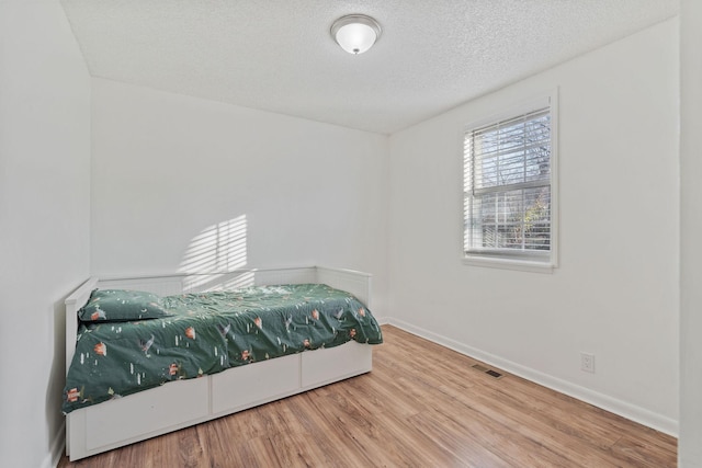 bedroom featuring visible vents, a textured ceiling, baseboards, and wood finished floors