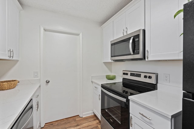 kitchen with white cabinets, stainless steel appliances, a textured ceiling, light countertops, and light wood-style floors