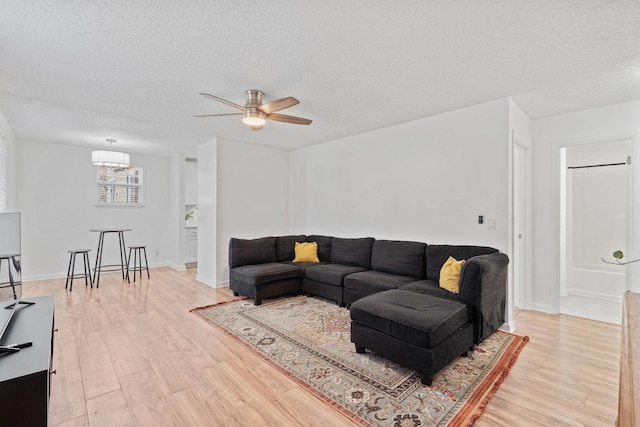 living room featuring a textured ceiling, baseboards, a ceiling fan, and light wood-style floors