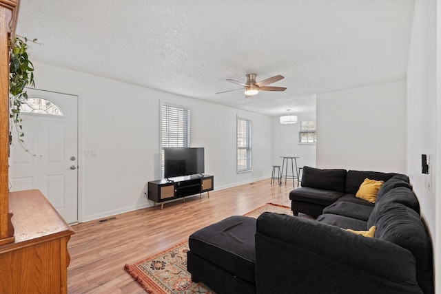 living area featuring baseboards, visible vents, light wood-style flooring, ceiling fan, and a textured ceiling