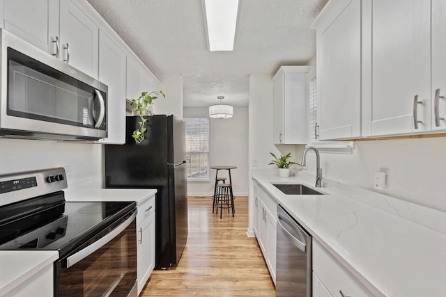 kitchen featuring light wood finished floors, white cabinets, appliances with stainless steel finishes, a textured ceiling, and a sink