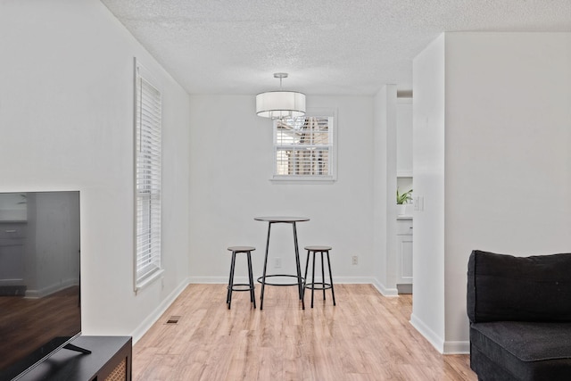 dining area with baseboards, light wood-style flooring, visible vents, and a textured ceiling