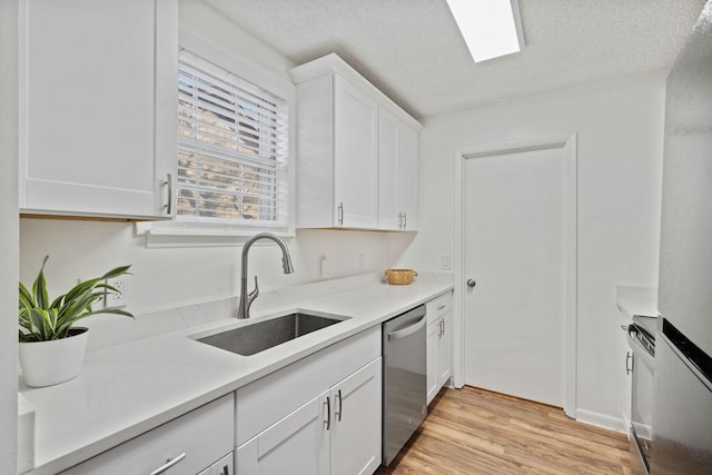 kitchen featuring light wood finished floors, a textured ceiling, stainless steel dishwasher, white cabinetry, and a sink