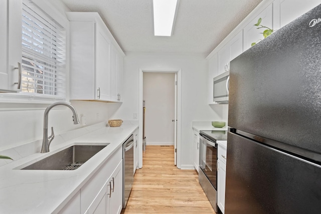 kitchen featuring light stone counters, light wood finished floors, appliances with stainless steel finishes, white cabinets, and a sink