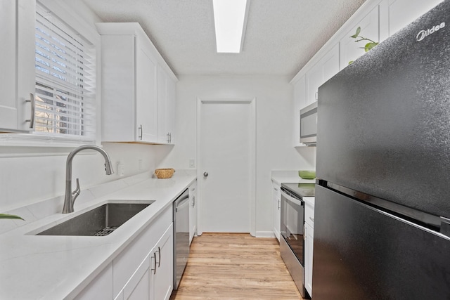 kitchen with stainless steel appliances, light wood-style floors, white cabinetry, a sink, and light stone countertops