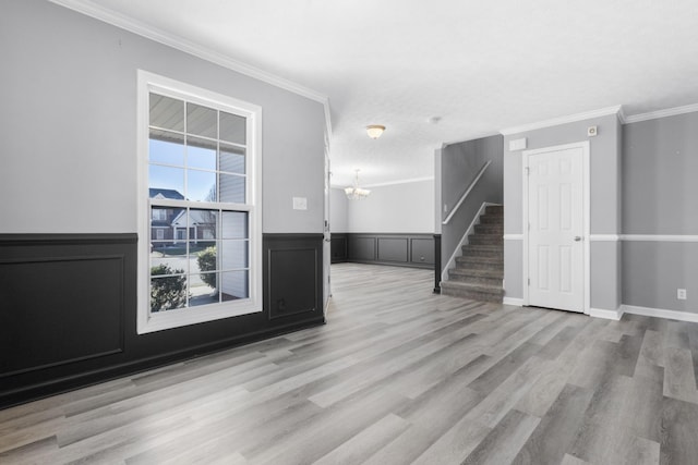 unfurnished room with a wainscoted wall, a notable chandelier, stairway, ornamental molding, and wood finished floors