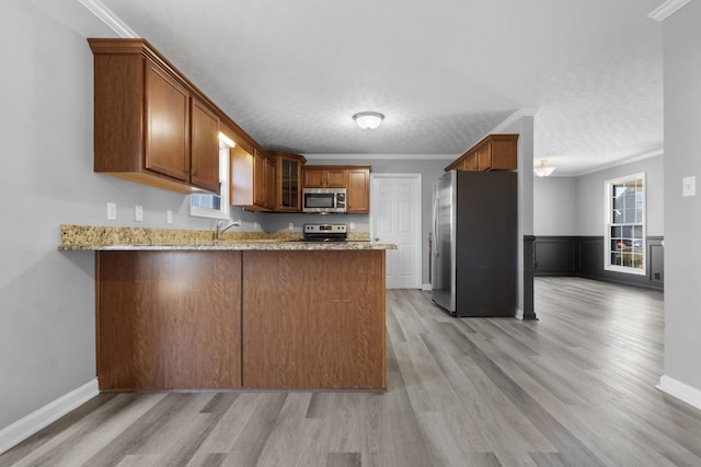 kitchen with light stone counters, crown molding, appliances with stainless steel finishes, a sink, and a peninsula