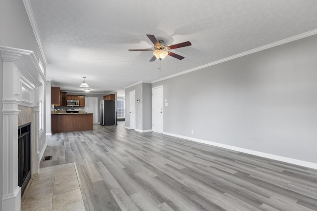 unfurnished living room featuring a textured ceiling, visible vents, baseboards, ornamental molding, and light wood-type flooring