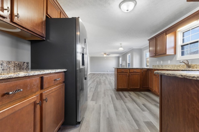 kitchen with stainless steel refrigerator with ice dispenser, brown cabinetry, a sink, light wood-type flooring, and a peninsula