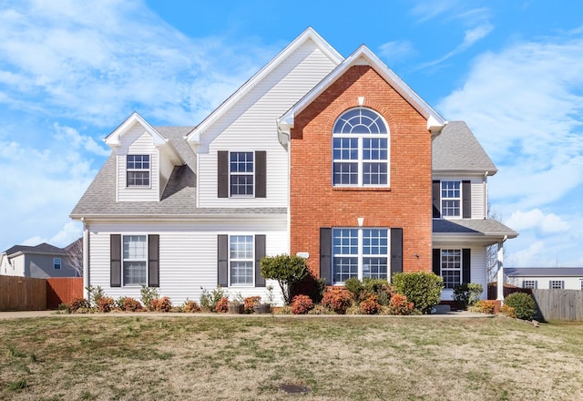 view of front of house with a front lawn, a shingled roof, fence, and brick siding