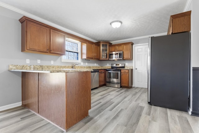 kitchen featuring a peninsula, appliances with stainless steel finishes, brown cabinetry, glass insert cabinets, and crown molding