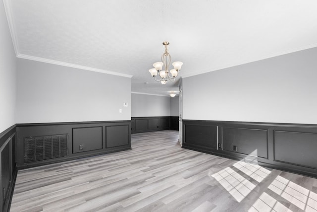 spare room featuring a wainscoted wall, visible vents, light wood-style floors, ornamental molding, and an inviting chandelier