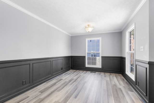 spare room with wainscoting, crown molding, visible vents, and light wood finished floors