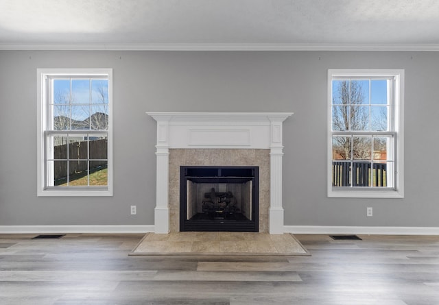 unfurnished living room with visible vents, baseboards, a fireplace with raised hearth, and wood finished floors