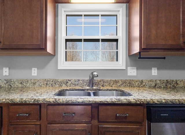 kitchen with light stone counters, dark brown cabinetry, a sink, and stainless steel dishwasher