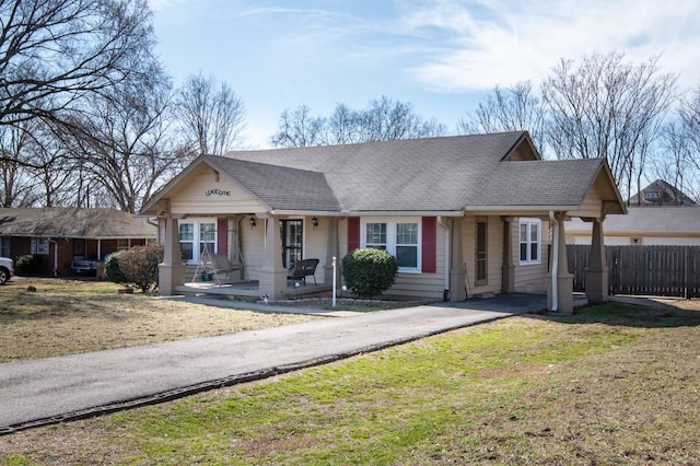 view of front of home with roof with shingles, fence, a porch, and a front yard