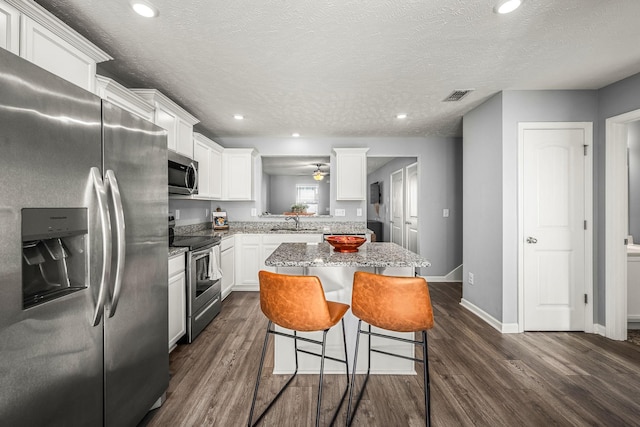 kitchen with dark wood-style floors, stainless steel appliances, visible vents, and a center island