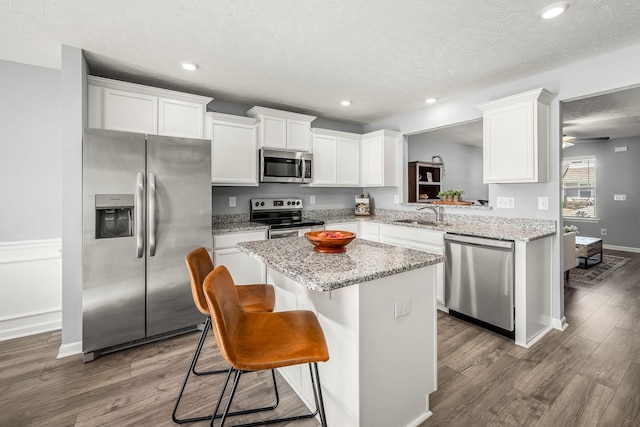 kitchen featuring appliances with stainless steel finishes, dark wood-type flooring, a kitchen island, and white cabinetry