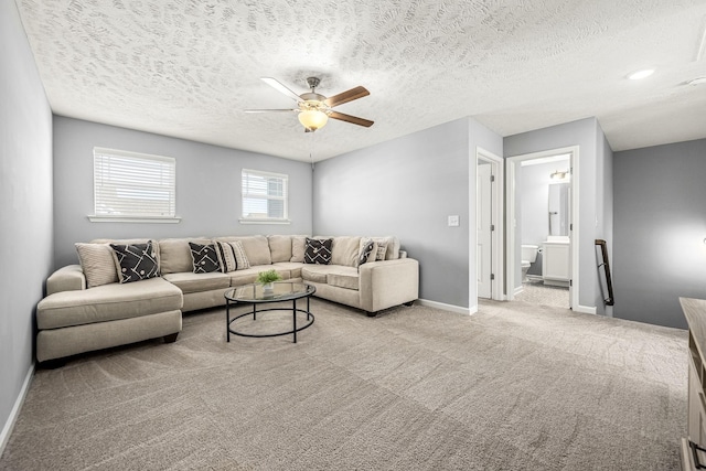 living room with baseboards, ceiling fan, a textured ceiling, and light colored carpet