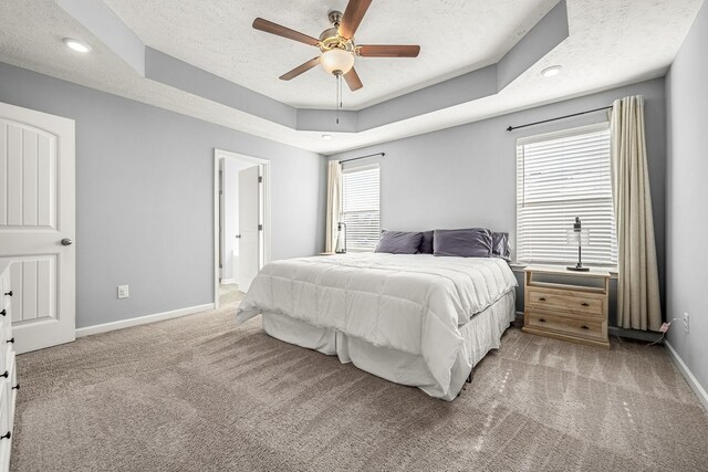 bedroom with a textured ceiling, connected bathroom, light colored carpet, baseboards, and a tray ceiling