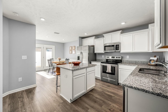 kitchen featuring appliances with stainless steel finishes, a center island, dark wood-type flooring, and a sink