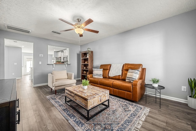 living room featuring ceiling fan, a textured ceiling, wood finished floors, and visible vents