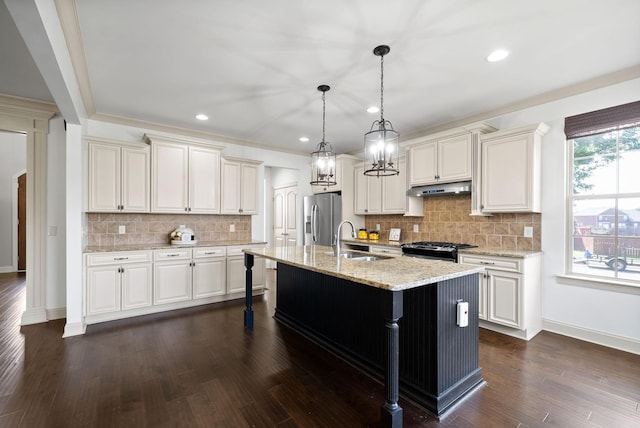 kitchen with light stone counters, a breakfast bar area, appliances with stainless steel finishes, a sink, and under cabinet range hood