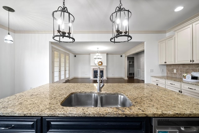 kitchen with light stone counters, a fireplace, crown molding, backsplash, and a sink