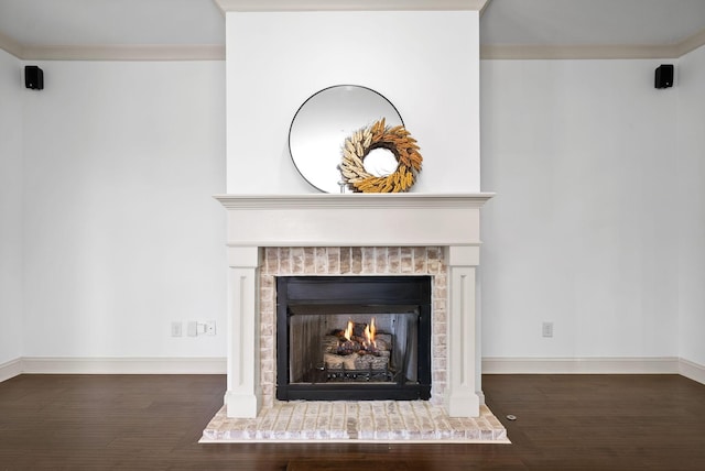 interior details featuring ornamental molding, a lit fireplace, baseboards, and wood finished floors