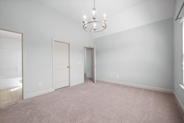 unfurnished bedroom with light carpet, baseboards, a chandelier, and ensuite bathroom