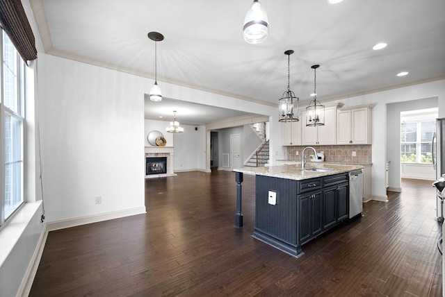 kitchen featuring a sink, stainless steel dishwasher, dark wood-style floors, tasteful backsplash, and a glass covered fireplace