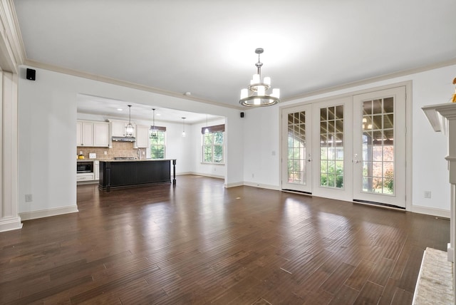 unfurnished living room with baseboards, a chandelier, and dark wood-style flooring