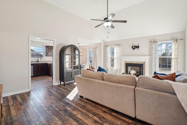 living room with dark wood finished floors, a ceiling fan, high vaulted ceiling, a tile fireplace, and baseboards