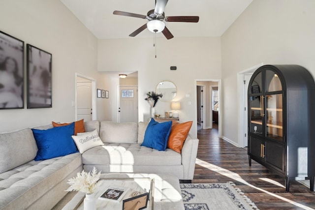 living room featuring a towering ceiling, baseboards, a ceiling fan, and wood finished floors