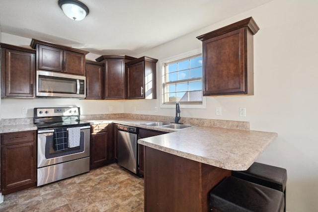 kitchen featuring appliances with stainless steel finishes, a kitchen breakfast bar, a peninsula, dark brown cabinets, and a sink