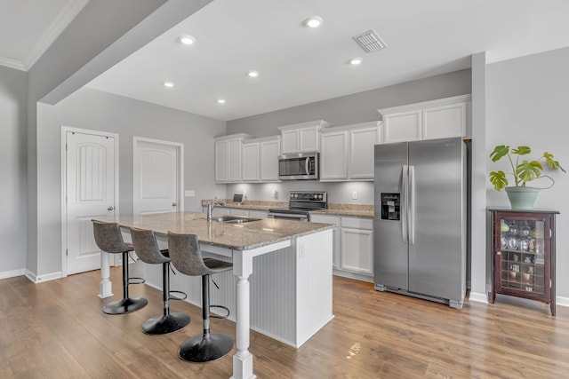 kitchen with visible vents, a kitchen breakfast bar, a kitchen island with sink, stainless steel appliances, and a sink